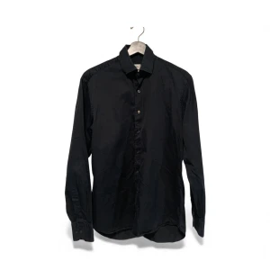 Svart skjorta från Stenströms, strl 40 - Svart skjorta från Stenströms i storlek 40 med fitted body-passform. Tillverkad i exklusiv twofold super cotton som känns mjuk och lyxig mot huden. Klassisk krage, knappar framtill och långa ärmar. Perfekt för dig som gillar stilrena och tidlösa plagg.