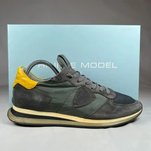 Philippe Model grå sneakers med gul detalj - Snygga sneakers från Philippe Model i grått med svart mesh framtill och gul häl. Skorna har en rund tå, platt sula och snörning. Materialmix av mocka, syntet och mesh ger en cool look. Perfekt för dig som gillar streetstyle och vill sticka ut med färgdetaljer. Kommer med skobox.