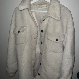 Vit teddyjacka från NLY Trend - Mysig vit teddyjacka från NLY Trend med stora bröstfickor och svarta knappar framtill. Finns en fläck där bak (se bild) men går att tvätta bort.