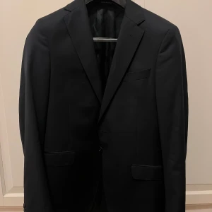 Mörkblå kavaj från Oscar Jacobson - Mörkblå fuego blazer ifrån Oscar Jacobsson. Varsamt använd och är fortfarande riktigt fin. Storlek 150 så längre i passformen. Hör gärna av dig vid frågor!