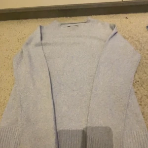 Ljusblå stickad kofta från Vero Moda - Mysig ljusblå stickad kofta från Vero Moda i storlek S. Koftan har lång ärm, öppen framtill och breda ribbade muddar vid ärmslut och nederkant. Perfekt att slänga på sig när det är lite kyligt ute. Superenkel att matcha med jeans eller kjol. Lite nopprig på sista bilden men jätte fin.