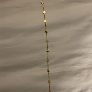 Guldigt halsband  med stjärnor - Snyggt halsband i guldton med små stjärnor längs hela kedjan. Perfekt för dig som gillar detaljer och vill ha något som sticker ut lite extra. Kedjan är tunn och smidig, och stjärnorna ger en cool och lekfull vibe. Passar till alla stilar och är lätt att matcha med andra smycken.