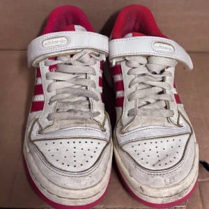 Adidas forum vit/röd retro - Säljer ett par klassiska Adidas Forum sneakers i vitt och rött med de ikoniska tre ränderna på sidan. Skorna har snörning, kardborreband och en cool retrostil. Yttermaterialet är skinn och insidan är fodrad i rött tyg. Sulan är röd med Adidas-logga undertill.