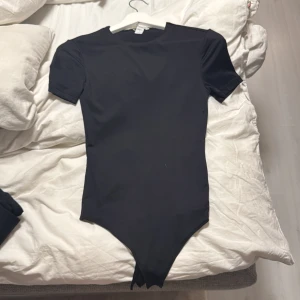 Svart kortärmad bodysuit från New yorker - En svart, tight body med korta ärmar och rund halsringning. Gjord i stretchigt material som sitter snyggt mot kroppen. Perfekt att styla med jeans eller kjol för en clean look. Använd 2 gånger