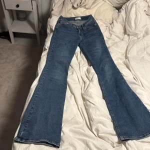 Blå bootcut jeans från Gina  - Säljer ett par klassiska blå jeans från Gina med bootcut-modell. Jeansen har normal passform upptill och utsvängda ben, perfekt för dig som gillar retrovibbar. Tillverkade i jeansmaterial med fem fickor och dragkedja framtill.