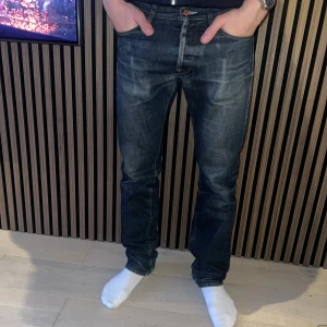 Mörkblå Acne Jeans 30/34 straight fit - Säljer ett par mörkblå jeans från Acne Jeans i modellen straight fit. Jeansen har klassisk femficksdesign, snygga slitningar och orangea sömmar. Tillverkade i 100% bomull och har en läderpatch med Acne Jeans-logga bak i midjan. Litet hål i greven.