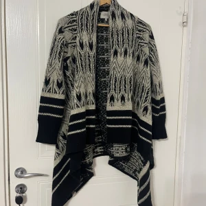 Svart och beige mönstrad kofta Papaya - Säljer en svart och beige kofta från Papaya Weekend i storlek S. Koftan har ett coolt grafiskt mönster, långärmade ärmar och en asymmetrisk, omlottliknande framkant. Materialet är mjukt och består av polyesterblandning. Perfekt för att ge din outfit lite edge.
