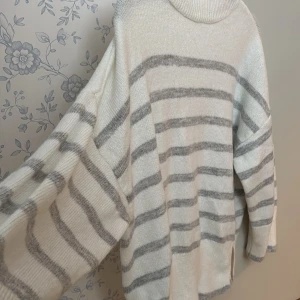 Vit och grå randig stickad tröja Ruechic - Supermysig stickad tröja från Ruechic i vitt med gråa ränder. Tröjan har en hög hals, lång ärm och en loose fit som ger en chill look .