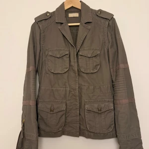 Grön jacka från Zadig & Voltaire - Snygg grön/grå från Zadig & Voltaire med fyra fickor framtill, axelklaffar och broderad logga på ärmen. Jackan har dragkedjor vid ärmsluten och markerade sömmar på ärmarna för en cool look. Köpte på vinted för 500kr men säljer pga att den är lite tight på mig. Storleken S men passar Xs samt Xxs 