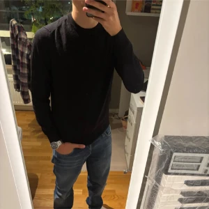 Svart långärmad tröja herr - En stilren svart långärmad tröja med rund hals. Passar perfekt till jeans och har en enkel, klassisk design utan synliga detaljer eller mönster. Tröjan har en normal passform och är ett måste i garderoben för dig som gillar minimalistisk stil.