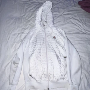 Moncler Jacka/hoodie - Snygg vit quiltad jacka från Moncler Grenoble med huva och dragkedja framtill. Jackan har ribbade muddar, två fickor med dragkedja och coolt Moncler-märke på bröstet. Perfekt för dig som vill ha en stilren och sportig look.