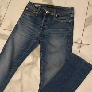 Blå jeans från Jack & Jones - Säljer ett par klassiska blå jeans från Jack & Jones med snygg tvätt och smal passform. Jeansen har fem fickor, gylf med dragkedja och läderpatch bak i midjan. Perfekta för dig som gillar en stilren och enkel look.