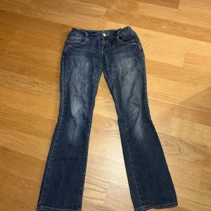 Blå bootcut jeans från Orsay, strl 36 - Snygga blå jeans från Orsay i bootcut-modell med dekorativa nitar vid fickorna och detaljerade bakfickor. Jeansen har klassisk femficksdesign och är tillverkade i jeansmaterial med en lätt tvättad look. Perfekta för dig som gillar en feminin och trendig stil.