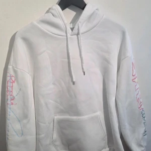 Vit hoodie med grafiskt graffiti tryck - En bekväm och stilren vit hoodie i mjukt material med borstad insida.  Mjuk och skön, påminner om fleece.  Byst: 95-101, Midja: 75-81, Höfter: 100-106