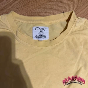 Gul t-shirt från Mambo - Snygg gul t-shirt från Mambo med tryck på bröstet i rött och svart. Klassisk rund halsringning och korta ärmar. Skön och lätt i bomull, perfekt för en avslappnad stil.