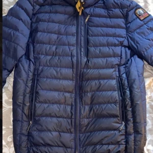 Blå dunjacka från Parajumpers S - Säljer en blå dunjacka från Parajumpers i storlek S. Jackan är superlätt, har quiltad design, hög krage med gul detalj och flera dragkedjor. Perfekt för kalla dagar och har en snygg patch på ärmen. Flera praktiska fickor med dragkedja.