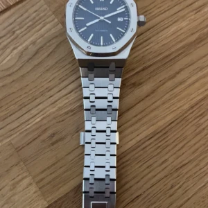 Seiko automatisk klocka  - Säljer en snygg Seiko automatisk klocka med åttakantig boett och länkarmband i borstat och polerat stål. Urtavlan är mörk med tydliga index och datumvisning. Baksidan har glas så du ser urverket. Riktigt stilren och modern design.