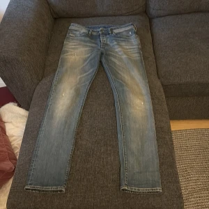 Blå jeans från Diesel, straight fit - Säljer ett par blå jeans från Diesel med snygga slitningar framtill och baktill. Jeansen har en rak passform och är tillverkade i jeansmaterial av bomull. Perfekta för dig som gillar en avslappnad och tidlös stil.