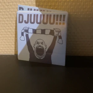 DJUUUU!!! Klibbor/ klistermärken  - En bok med ett energiskt omslag som visar en supporter som håller upp en halsduk och ropar DJUUUU!!! Perfekt för dig som älskar sport, fanskultur och vill ha något unikt i bokhyllan. Passar ungdomar och unga vuxna som gillar att sticka ut och visa sin passion.