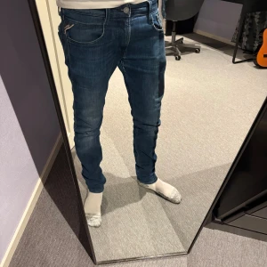 Replay Anbass slim fit jeans blå - Säljer ett par snygga Replay Anbass slim fit jeans i klassisk blå tvätt. Jeansen har fem fickor, diskreta slitningar och en smal passform som sitter tajt men ändå bekvämt. Perfekta för dig som gillar en modern och stilren look. Storlek w31 L32