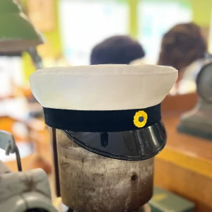 Klassisk Studentmössa 52-63 - Klassisk studentmössa med vit ovandel i bomull, svart sammetsband och blank svart skärm. Framtill sitter en gul broderad knappdetalj. Insidan har foder i blått och gult, inspirerat av svenska flaggan. Perfekt för studenten och högtidliga tillfällen.Skriv till oss vilken storlek det är du vill ha