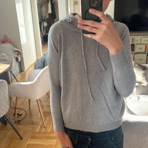 Grå hoodie med huva och snörning - Säljer en stilren grå hoodie med huva och snörning. Tröjan har långa ärmar, ribbade muddar och är tillverkad i mjukt material som känns skönt mot huden. Perfekt för en chill och avslappnad look. Modellen är 172 