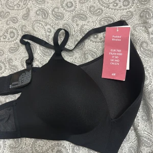 Svart padded linnetopp/BH från H&M - Svart linnetopp från H&M med vadderade kupor och tunna axelband. Toppen är wireless och har meshdetaljer på sidan för extra komfort och snygg look. Stilren och enkel design som funkar till många outfits. Aldrig använd.