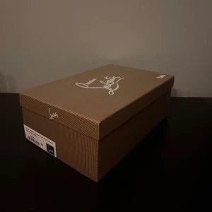 Grå mocka sneakers från Louboutin - Säljer ett par grå sneakers från Christian Louboutin i mjuk mocka med klassisk röd sula och vita platta sulor. Skorna har rund tå, snörning och diskreta detaljer. Insidan är beige och ger en lyxig känsla. Perfekt för dig som gillar stilrena och exklusiva sneakers.