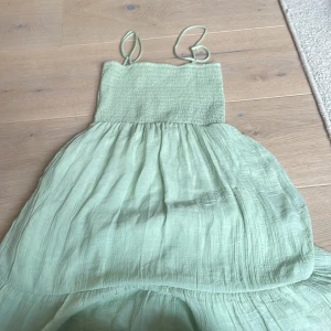 Ljusgrön sommarklänning från FB Sister - Superfin ljusgrön klänning från FB Sister i storlek XXS. Klänningen har smala axelband, smockad överdel och ett luftigt, vågigt kjolparti. Perfekt för varma dagar och ger en fräsch och trendig look.