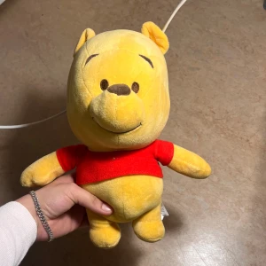 Winnie the Pooh talande gosedjur - Mysig Winnie the Pooh-gosedjur från Disney med röd tröja. Tryck på handen för ljudfunktion ("Press Me"). Bra skick, inga synliga fläckar eller skador. Perfekt för barn eller samlare av Disney-produkter. Priset kan diskuteras!!!