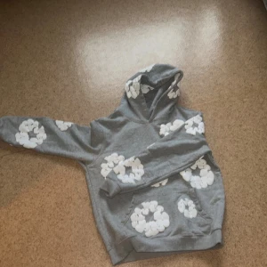 Grå denim tears hoodie  - En grå denim tear hoodei. Tröjan har huva och en klassisk känguruficka framtill. Perfekt för dig som gillar en chill och trendig stil med lite extra detaljer.