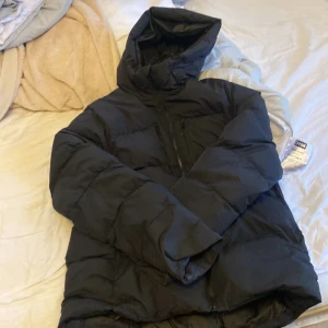 Svart pufferjacka från Everest M - Säljer en svart pufferjacka från Everest i storlek M. Jackan har huva, dragkedja framtill och en bröstficka med dragkedja. Perfekt för kalla dagar och riktigt skön att bära. Klassisk och enkel design som funkar till det mesta. Den Säljs för den är liten på mig 