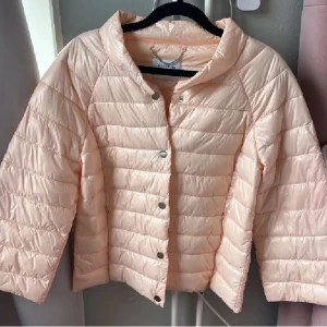 Ljusrosa pufferjacka med trekvartsärm - Snygg ljusrosa pufferjacka med trekvartsärm och knappar framtill. Jackan har en lätt vadderad känsla och en feminin passform. Perfekt för vår eller kyliga sommarkvällar. Enkel och stilren design.💞💞 Passar både XS och S super bra.😊