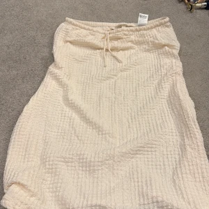 Beige långkjol från H&M med snörning - Luftig beige långkjol från H&M i strukturerad, krinklad polyesterblandning. Kjolen har resår och snörning i midjan för en bekväm passform. Perfekt för dig som gillar en enkel men trendig stil.