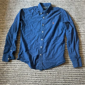 Blå skjorta från Polo Ralph Lauren - Säljer en blå/mörkblå skjorta från Polo Ralph Lauren i slim fit. För mer bilder eller frågor är det bara att hör av sig. Den är storlek M men passar även S. 