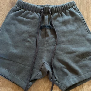Grå Essentials Fear of God shorts XS - Snygga grå shorts från Essentials Fear of God i mjuk bomull med elastisk midja och långa snören framtill. Klassisk loose fit och diskret logga på benet. Perfekta för chill dagar eller streetwear-stil.Byten går också😀