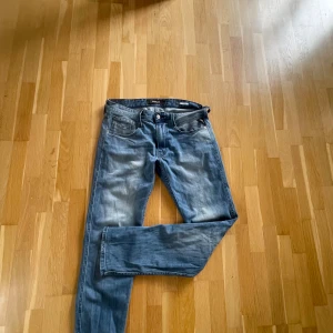 Blå Replay jeans straight fit - Snygga blå jeans från Replay med klassisk femficksdesign och diskreta slitningar. Jeansen har raka ben och normal passform, perfekt för en avslappnad stil. Tydliga Replay-detaljer på bakfickan och läderpatch i midjan. Tillverkade i mjukt denimtyg.