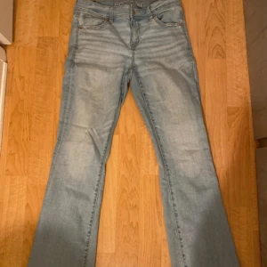 Bootcut jeans från American Eagle - Ljusblå bootcut jeans från American Eagle med klassisk femficksdesign och låg midja. Jeansen har en snygg tvättad look och är tillverkade i mjukt denimtyg som sitter skönt på kroppen. Perfekta för dig som gillar en avslappnad men trendig stil.