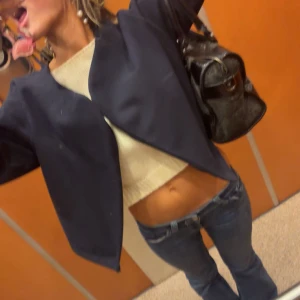 Mörkblå croppad kavaj Gina - Snygg mörkblå kavaj från Monki med croppad passform och öppen framtill. Jackan har lång ärm och är tillverkad i ett mjukt material som känns lite som ull. Perfekt för dig som vill ha en stilren och trendig look.