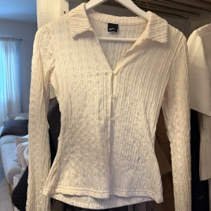 Vit crinklad skjorta från Gina Tricot - Säljer en vit, crinklad skjorta från Gina Tricot med klassisk krage och knappar framtill. Skjortan har lång ärm och är tillverkad i ett lätt, strukturerat tyg som ger en cool och trendig look. Använd 1 gång, i bra skick.