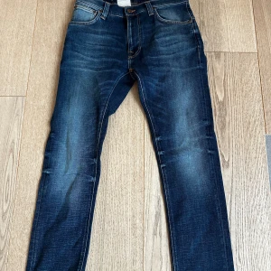 Nudie Jeans Thin Finn Indigo Dreams W30 L28 - Helt nya alldrig använda. Snygga blå jeans från Nudie Jeans, modell Thin Finn Indigo Dreams. Jeansen har en smal passform med klassisk femficksdesign, orangea sömmar och läderpatch bak. Tillverkade i ekologisk bomull med stretch för extra komfort. Perfekt tvättad blå färg med slitningar. 