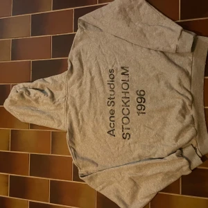 Grå hoodie från Acne Studios - Säljer en grå hoodie från Acne Studios med tryck 'Acne Studios STOCKHOLM 1996' på ryggen. Klassisk modell med huva och långa ärmar, tillverkad i mjuk bomull. Perfekt för en chill och stilren look. Strl S enligt tag men sitter mer som M! Ni vet varför den är så billig!