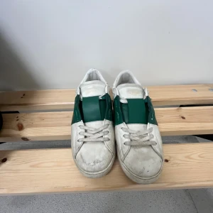 Valentino Open sneakers vit/grön skinn - Säljer ett par Valentino Open sneakers i vitt skinn med bred grön läderdetalj över mitten. Klassisk rund tå, snörning och platt sula. Märkeslogga på plösen och diskret branding på sidan. Perfekta för dig som gillar stilrena men ändå unika sneakers. Pris kan diskuteras 