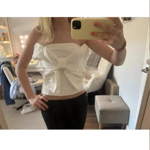 Vit axelbandslös tubtopp med stor rosett - Supersöt vit tubtopp med en stor, iögonfallande rosett framtill. Toppen är axelbandslös och har en croppad passform som ger en trendig look. Perfekt för dig som vill sticka ut med en unik och stilren topp. Materialet känns mjukt och lätt mot huden.