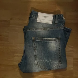 Dsquared2 blå slitna jeans - Säljer ett par blå jeans från Dsquared2 med coola slitningar och patchade detaljer. Jeansen har en klassisk femficksmodell, normal passform och snyggt tvättad finish med ljusa partier. Hör av dig vid frågor o funderingar 