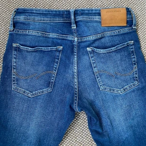 Jack & Jones Slim fit jeans  - Snygga blå jeans från Jack & Jones med klassisk femficksdesign och läderpatch bak i midjan. Jeansen har slimfit passform och diskreta slitningar framtill för en cool look. Tillverkade i stretchig denim för extra komfort.     Storlek: W29 L30