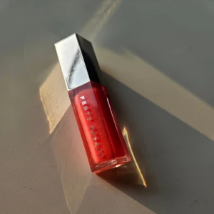 Fenty Beauty rött läppglans - Snyggt läppglans från Fenty Beauty i limited edition färgen dragon mami  med glansig finish och lätt skimmer. Kommer i en stilren, sexkantig plastförpackning med silvrigt lock. Perfekt för att ge läpparna en pop av färg och glans. Testad men föredrar mer dova färger🙂