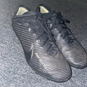 Nike Mercurial fotbollsskor svarta - Säljer ett par svarta Nike Mercurial fotbollsskor med snörning och Zoom-dämpning. Skorna har en modern, strömlinjeformad design med syntetmaterial och tydliga Nike-loggor. Perfekta för dig som vill ha grymt grepp på planen och snygg look.
