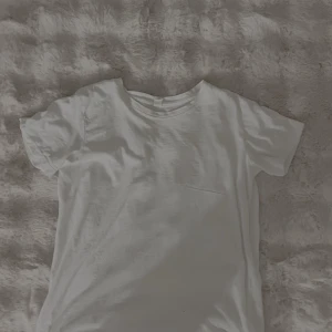 Vit basic t-shirt från Åhléns - En klassisk vit t-shirt från Åhléns Woman i storlek S. T-shirten har rund halsringning och korta ärmar, perfekt för en clean och enkel stil. Tillverkad i mjuk bomull som känns skön mot huden.