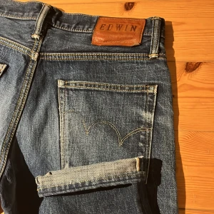 Edwin 53RV blå jeans selvedge - Snygga blå jeans från Edwin, modell 53RV, tillverkade i Japan. Klassisk femficksdesign med kontrastsömmar och läderpatch bak i midjan. Jeansen har rak passform och är gjorda i 100% bomull för en autentisk denimkänsla. Selvage och passar mer som 31 eller 32 i längd